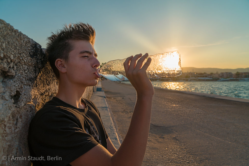 young man drinking water with the sun behind the bottle