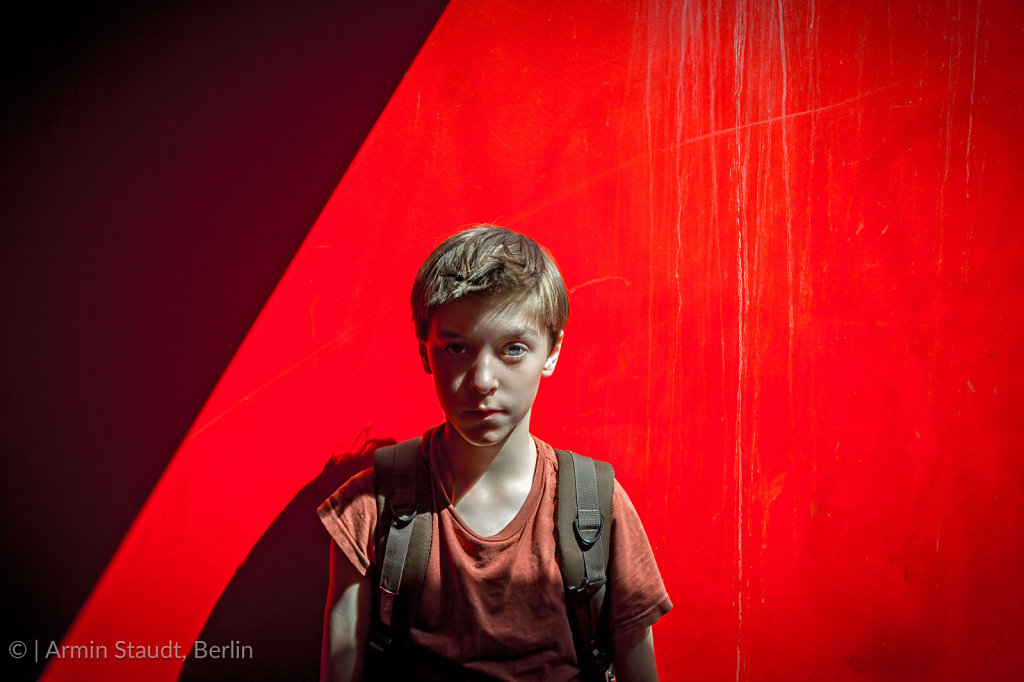 portrait of a teenager boy with rucksack in front of a red wall, with strong shadows