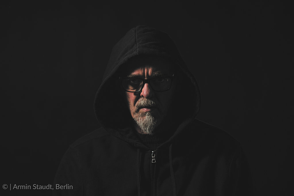 dark portrait of a man with gray beard , hoodie and glasses